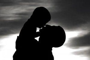 A statue of a father kissing his son, silhouetted against a bright winter sun. Statue in bronze by Olof Ahlberg, 1921.